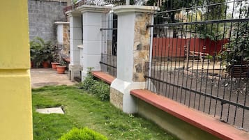 A fenced outdoor area with a grassy lawn, potted plants, and a stone wall.