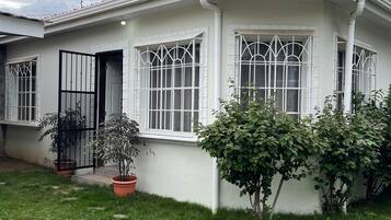 A two-story house with a tiled roof, large windows with metal bars, and a paved front yard with potted plants.