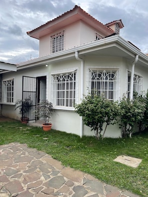 A two-story house with a tiled roof, large windows with metal bars, and a paved front yard with potted plants. - Tropical Oasis in Managua (Nindiri)