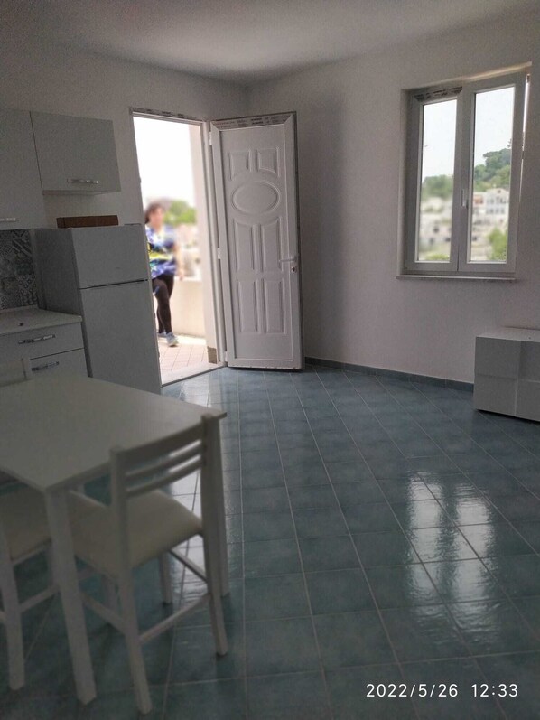 Ein Zimmer mit Esstisch, Stühlen, einem Kühlschrank und einer Tür, die nach draußen führt.