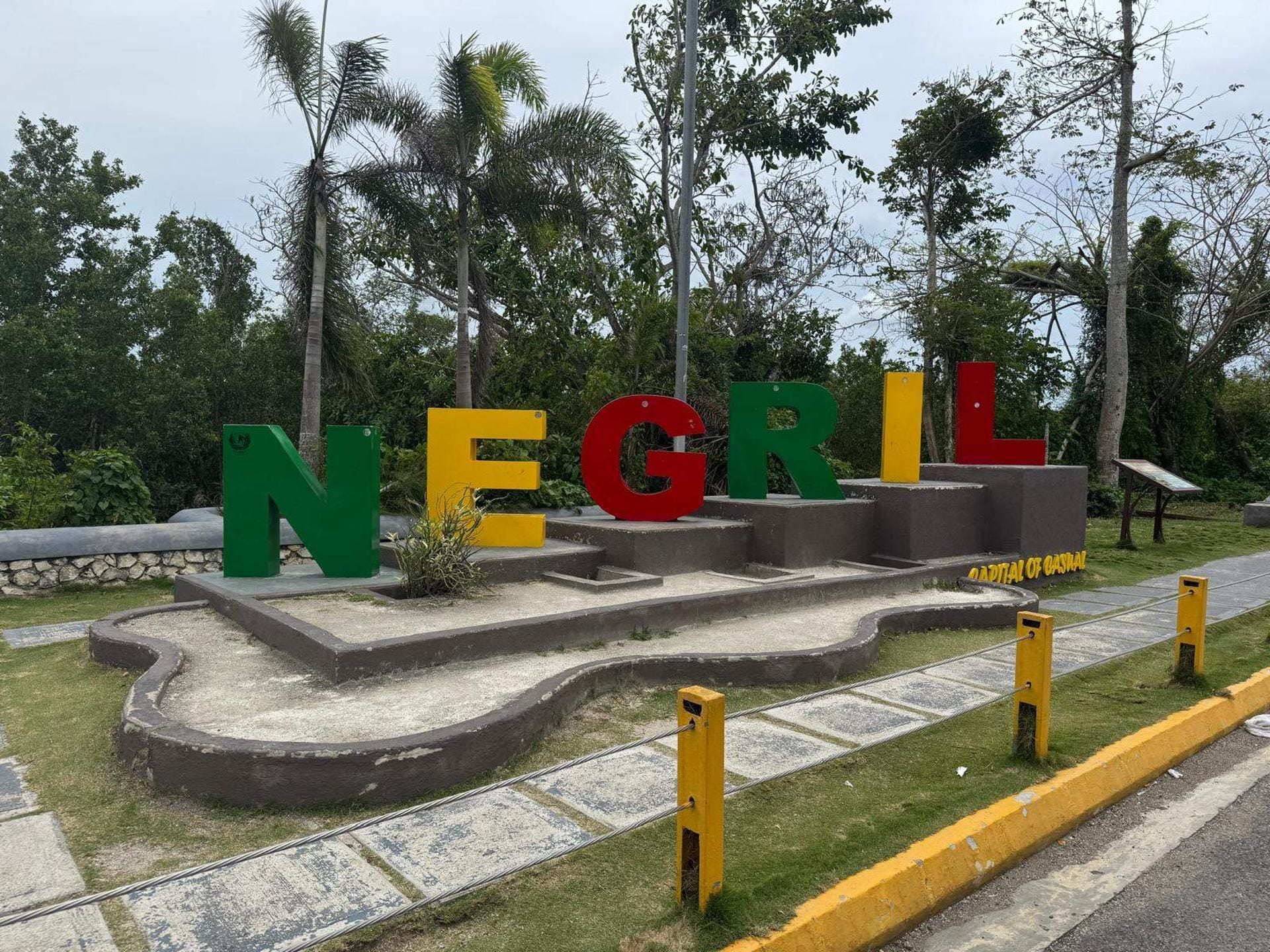 A sign with the letters 'NEGRI' in different colors, surrounded by greenery and a paved area.