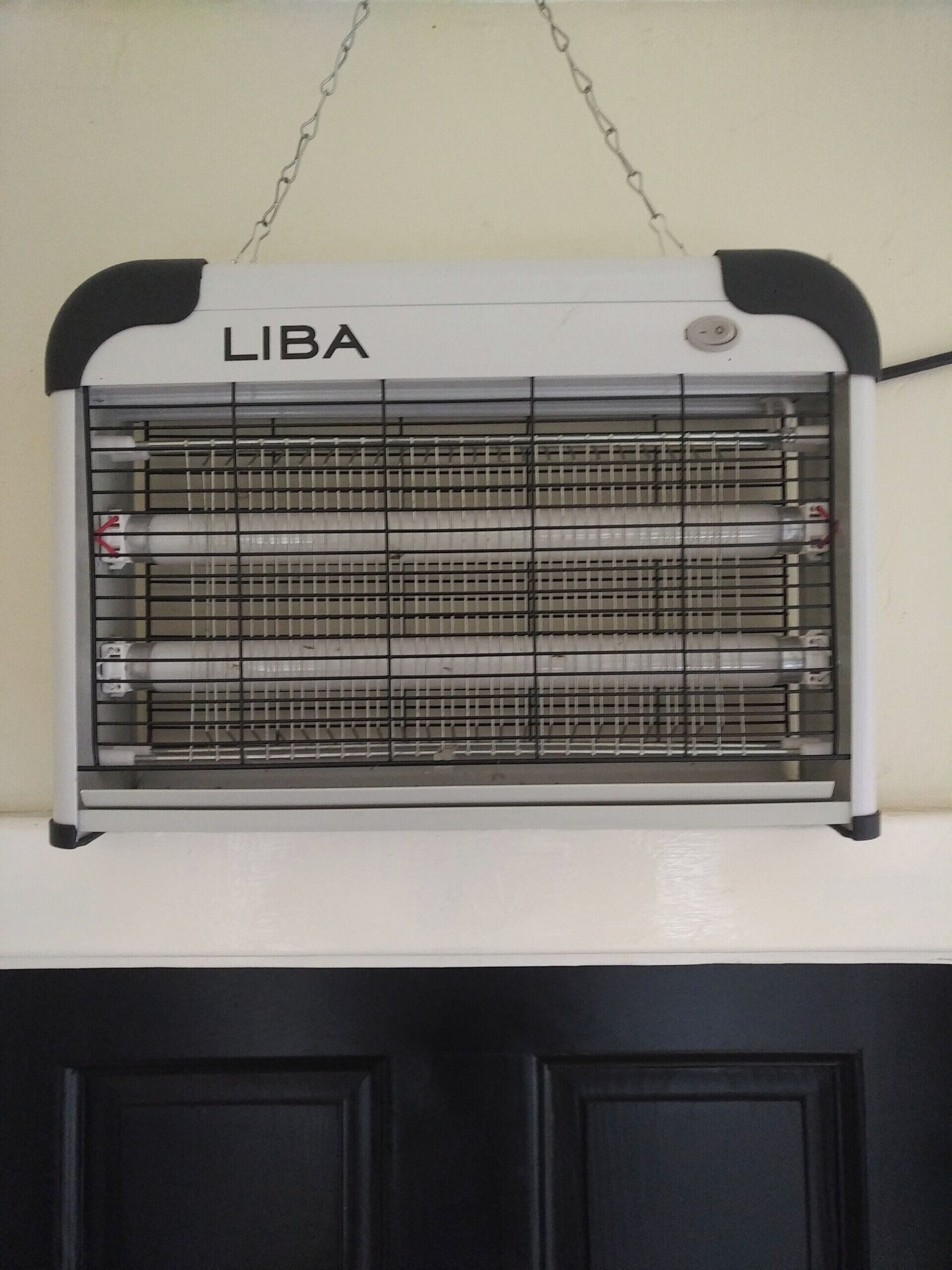 A window with a metal grill and the word 'LIBA' on it, mounted above a black door.