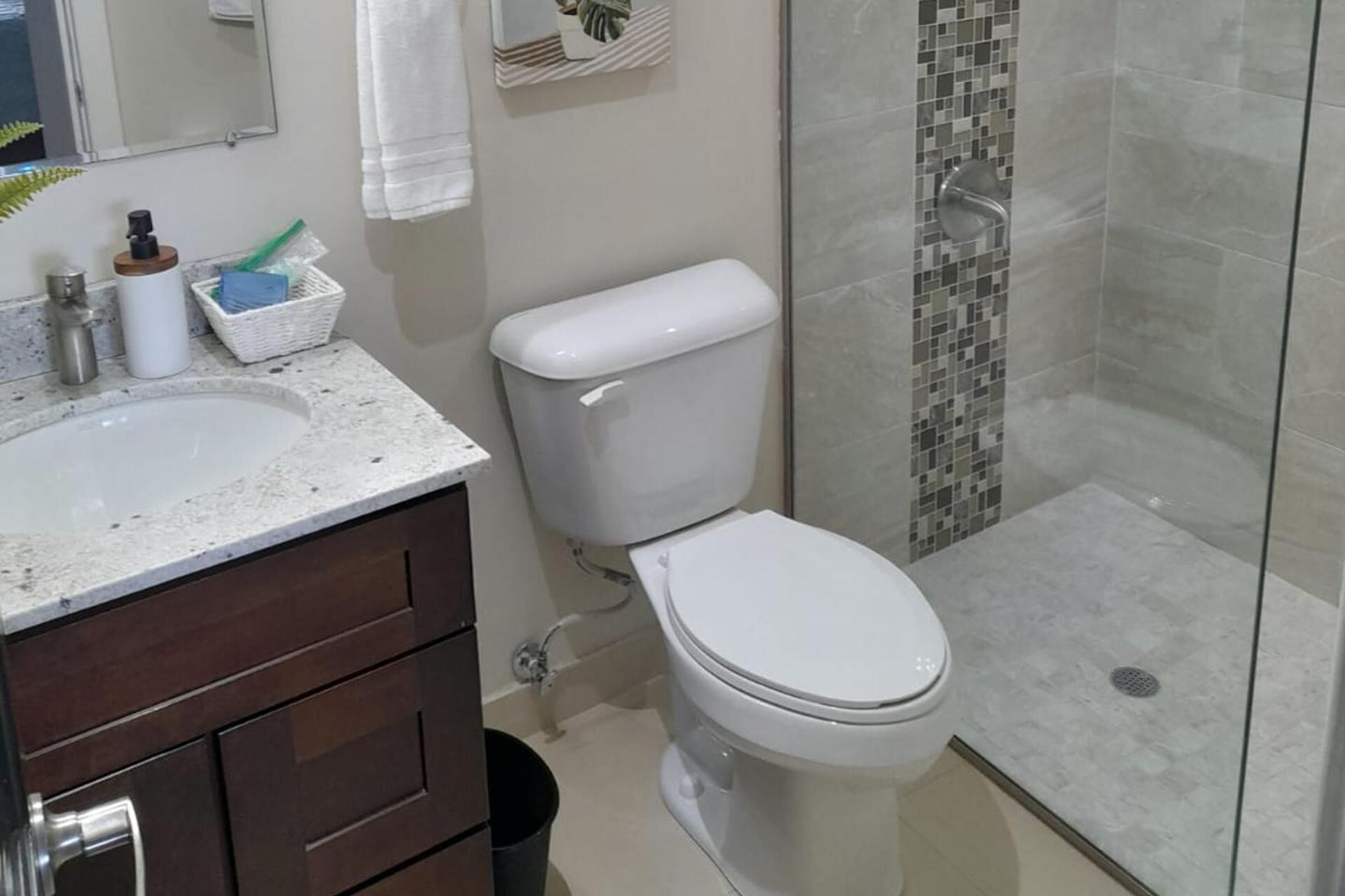 Et badeværelse med toilet, vask med marmorplade og bruseafsnit med glasdør.