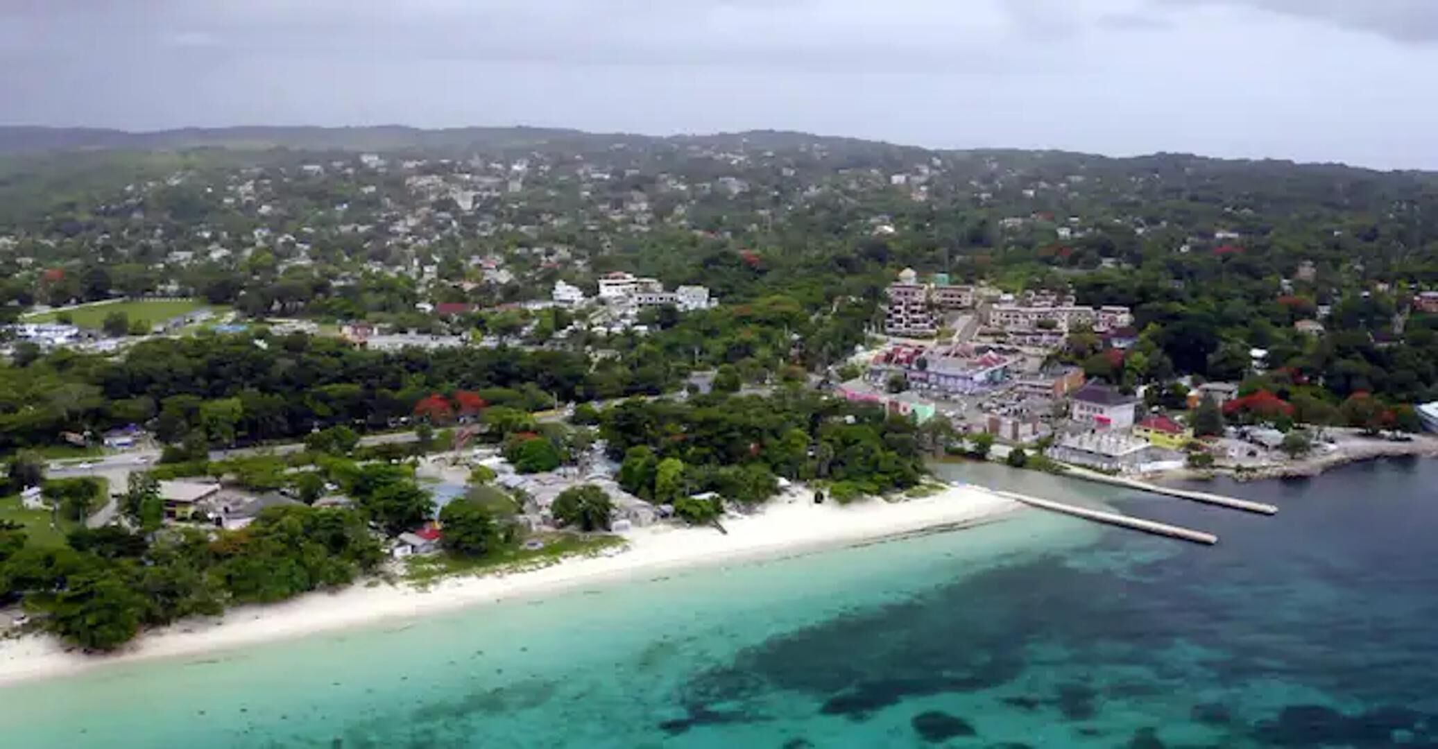 An aerial view of a coastal town with a beach, buildings, and a pier.