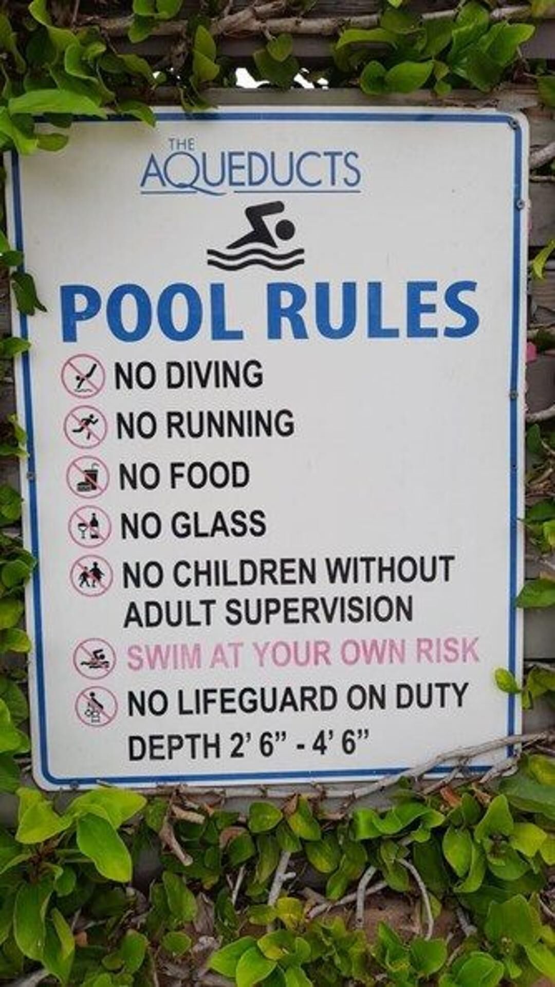 A sign with pool rules including no diving, no running, no food, no glass, no children without adult supervision, swim at your own risk, no lifeguard on duty, and depth limits.