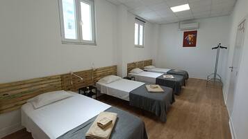 A hotel room with four single beds, a wooden headboard, a standing heater, and a window with blinds.