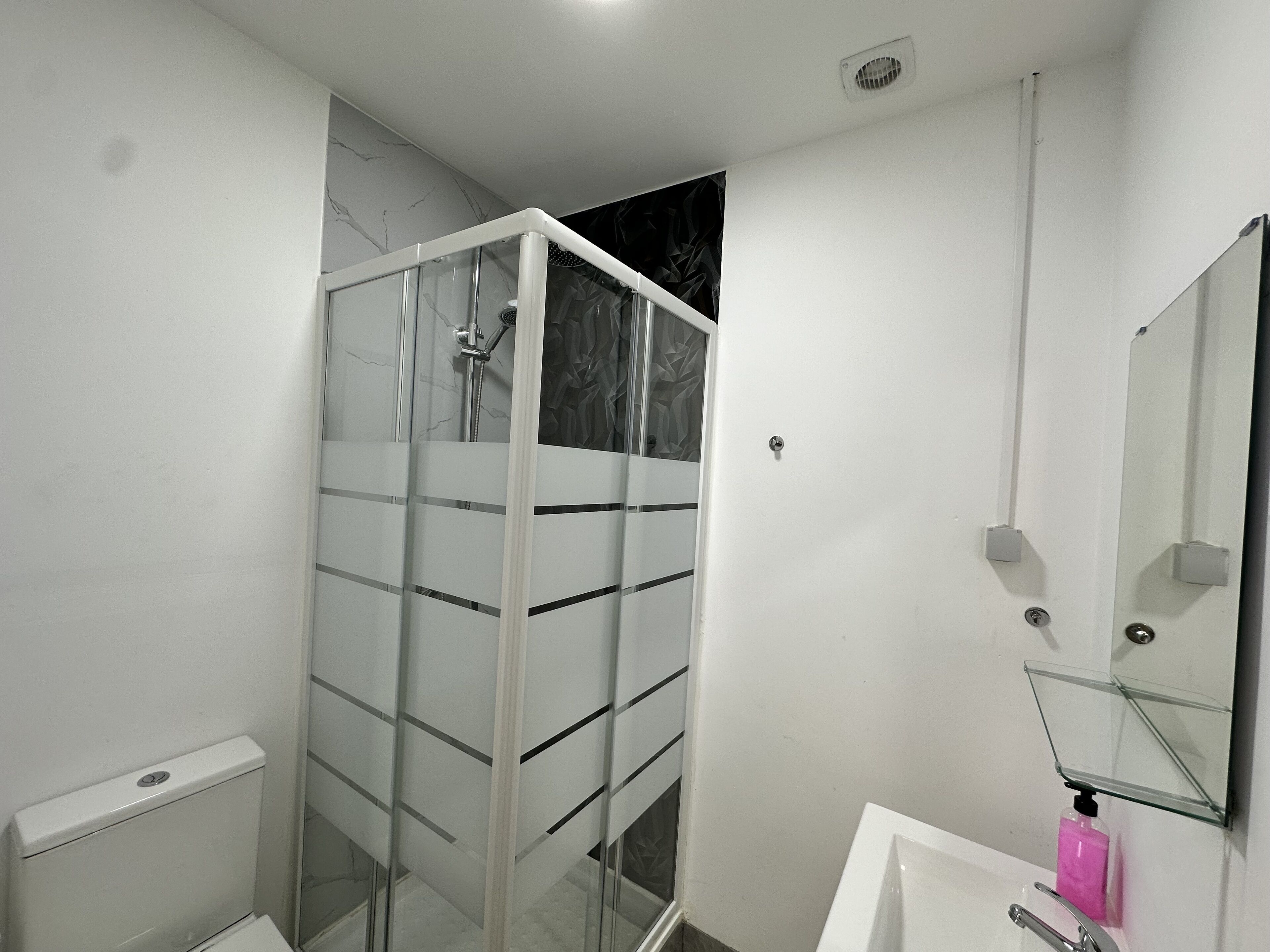 A modern bathroom with a glass shower enclosure, a white sink with a mirror, and a soap dispenser.