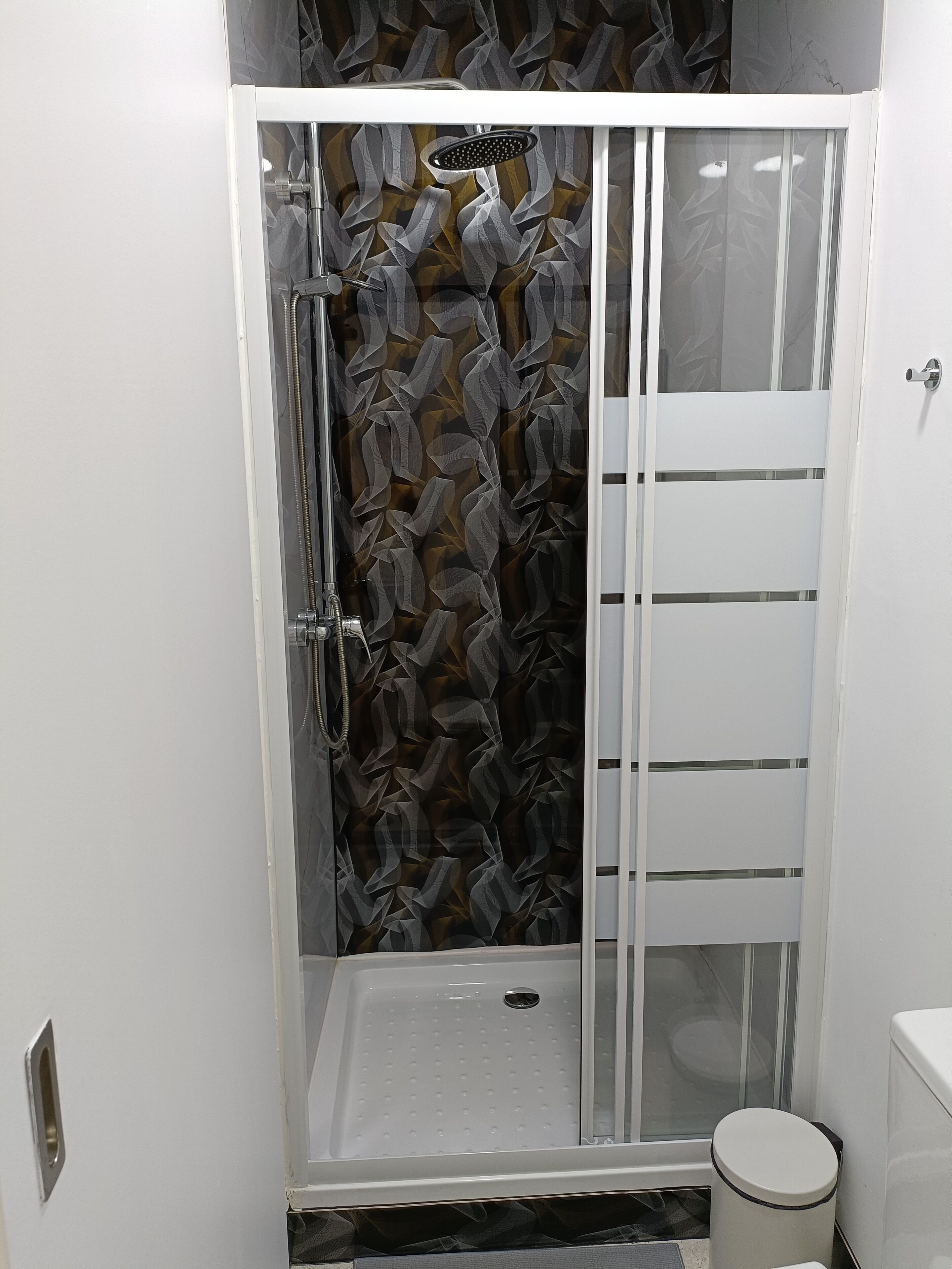 Una cabina doccia con porta in vetro, un soffione e pavimento piastrellato.