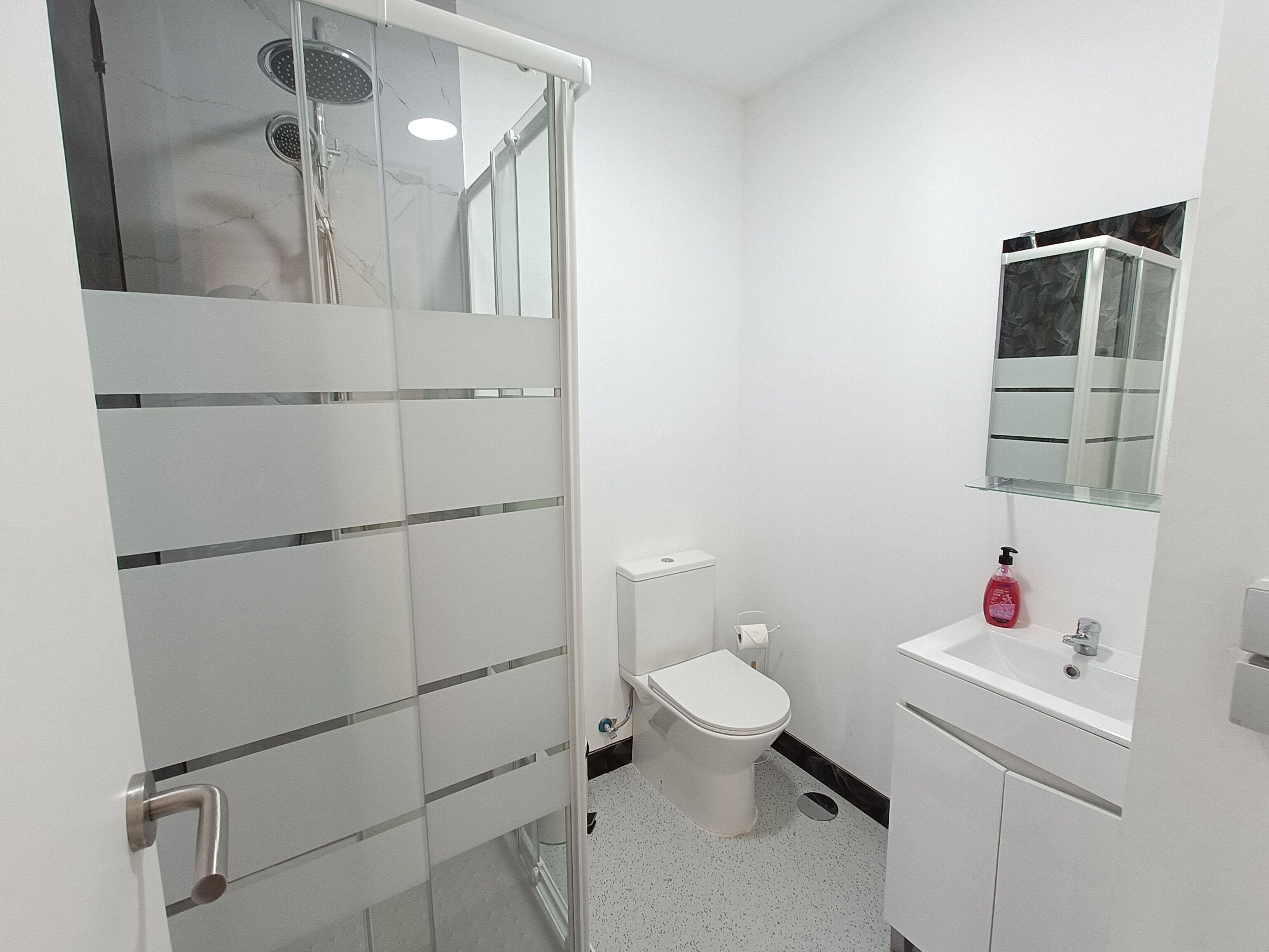 Ein modernes Badezimmer mit Duschkabine aus Glas, Toilette und Waschbecken mit Spiegel darüber.