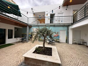 An outdoor courtyard with a central tree planter, outdoor seating, and a mural on the wall. - Albergaria Formosa (Faro)