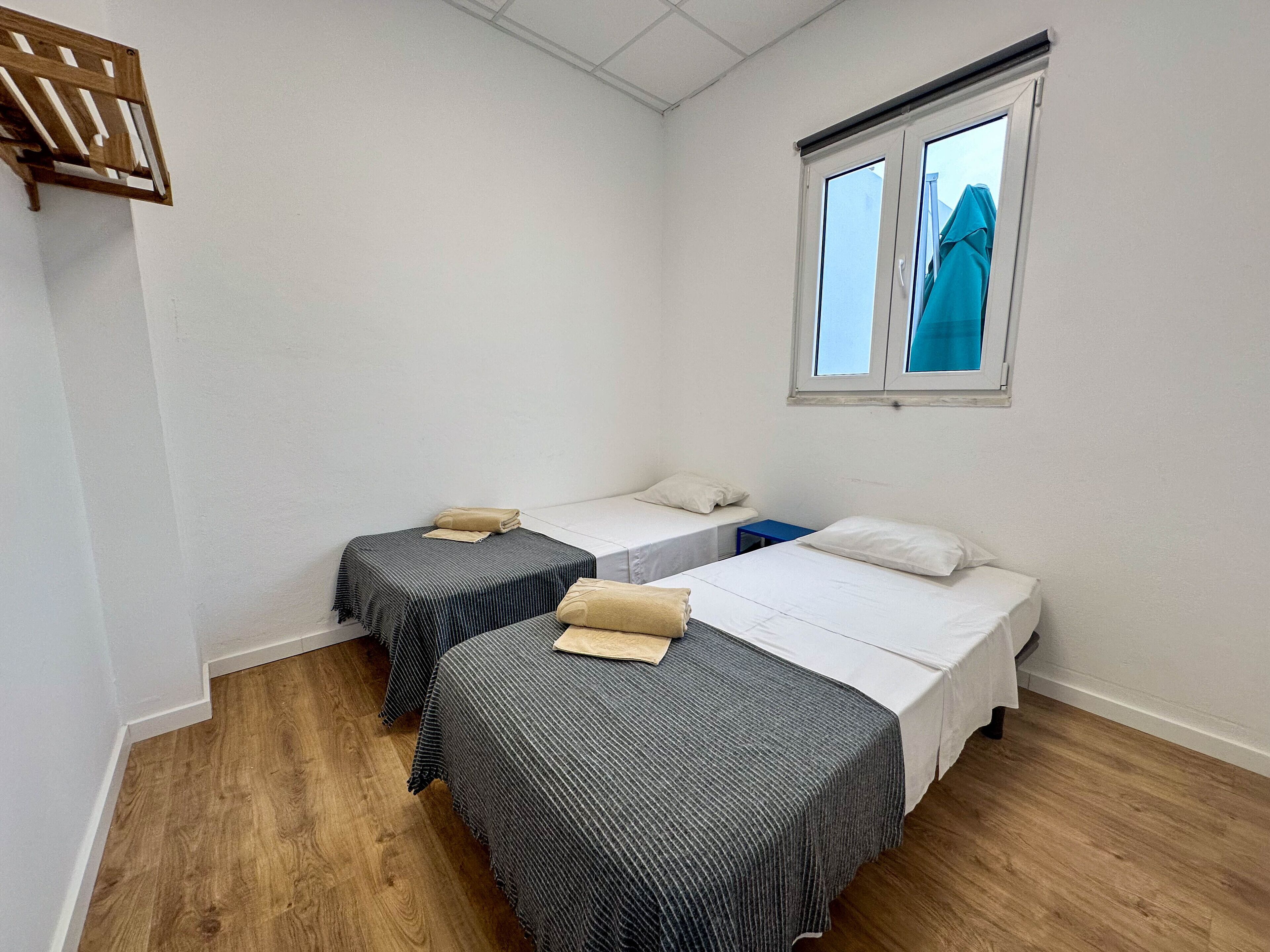 Une chambre avec deux lits simples, une petite table et une fenêtre avec des stores.