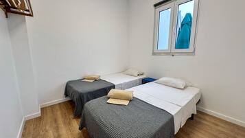 A room with two single beds, a small table, and a window with blinds.