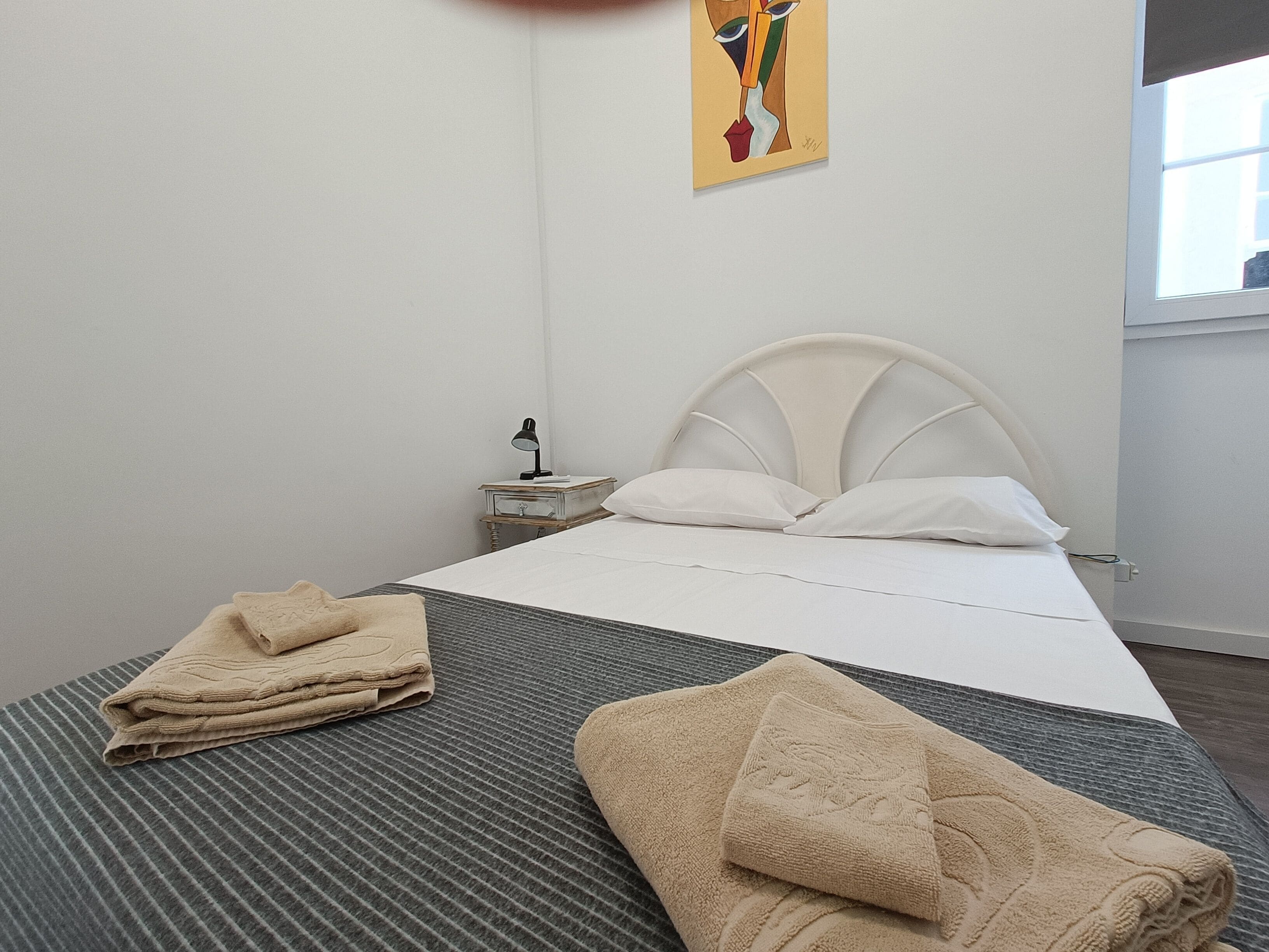 A neatly made bed with white linens, a headboard, and a bedside table with a lamp.