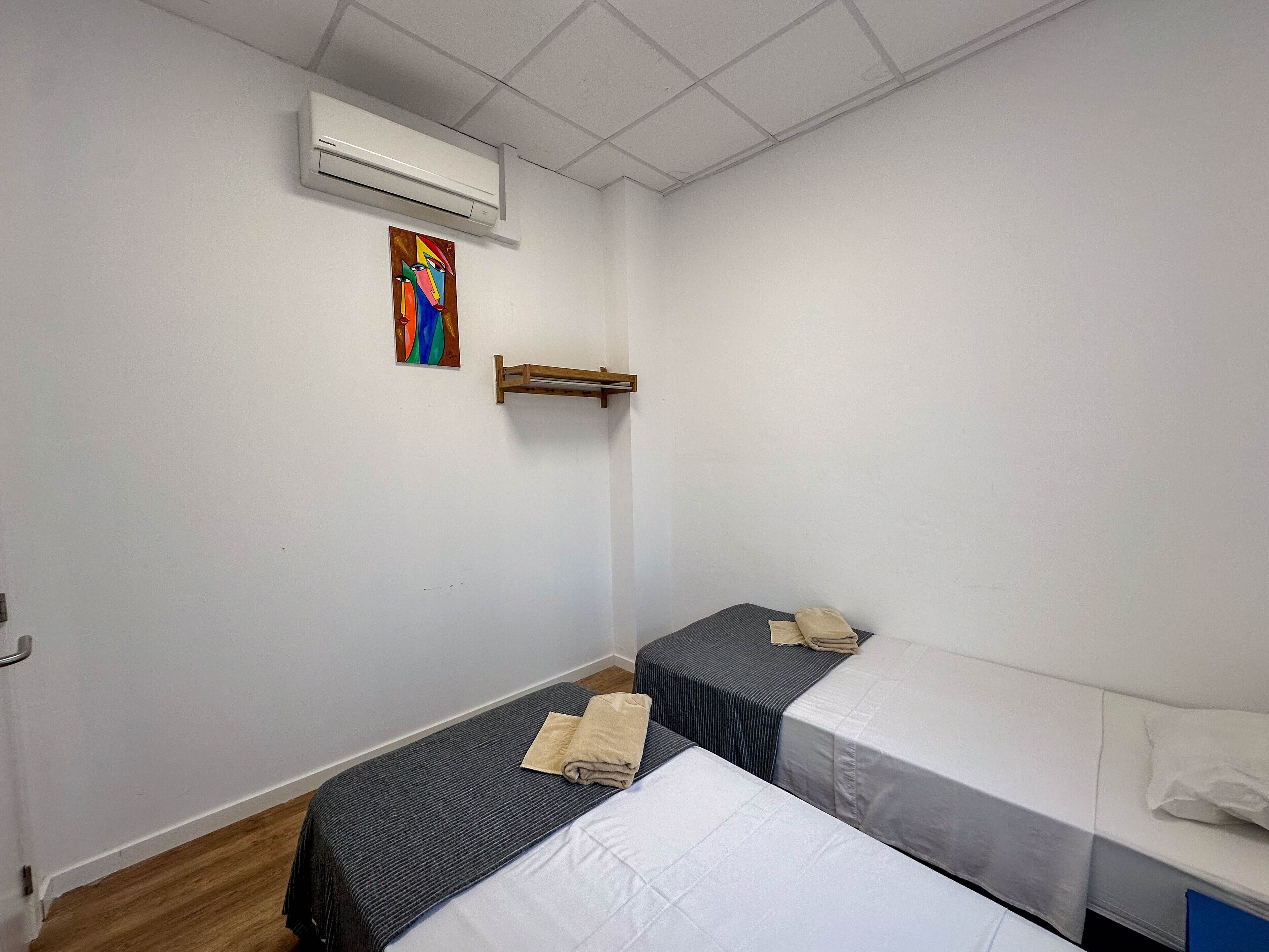 A room with two beds, a painting on the wall, and an air conditioning unit.