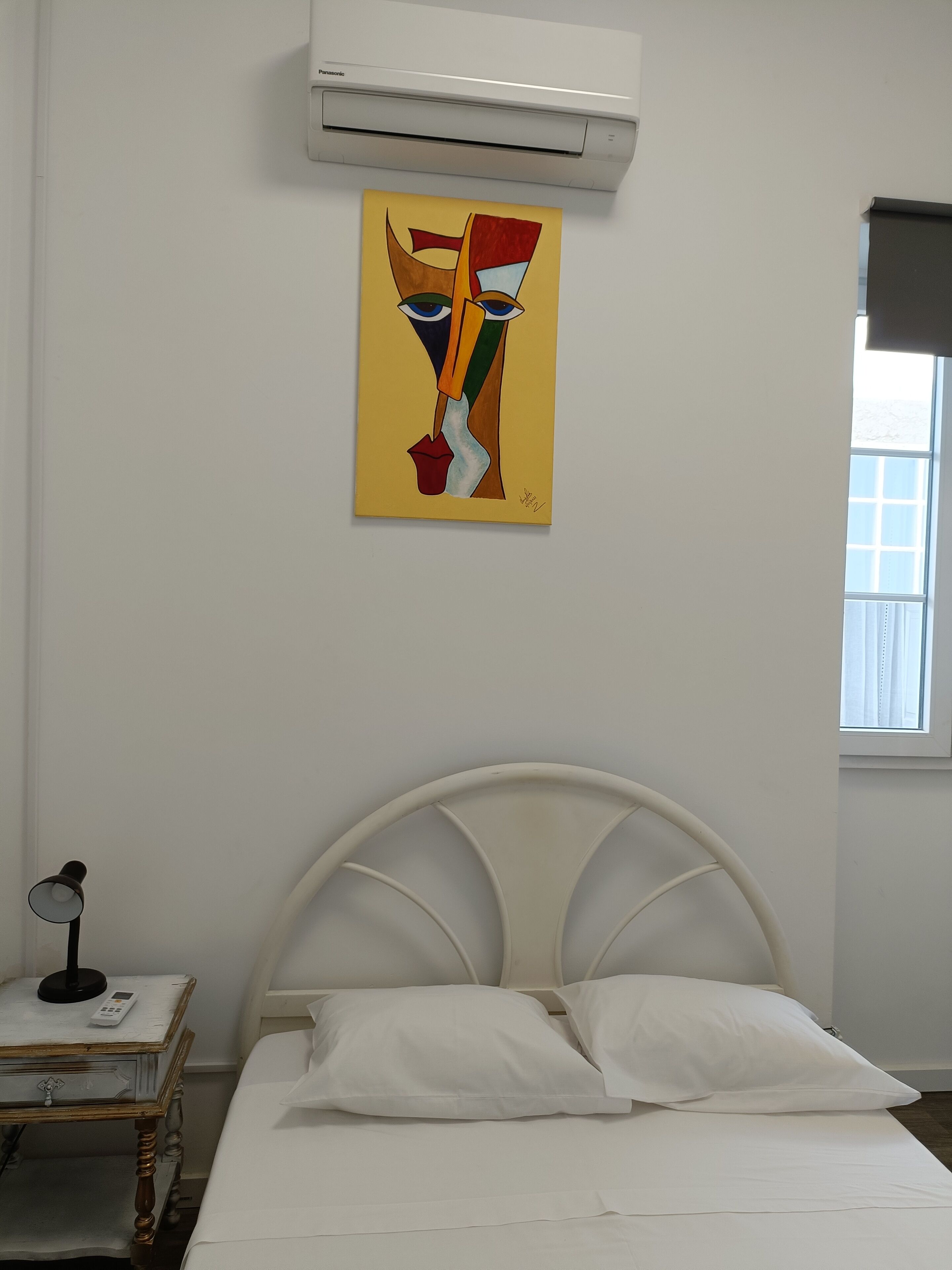 Une chambre à coucher avec un lit blanc, une table de chevet avec une lampe et un tableau accroché au mur.