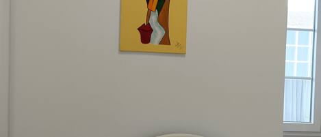 Une chambre à coucher avec un lit blanc, une table de chevet avec une lampe et un tableau accroché au mur.