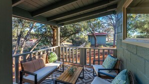 A covered outdoor seating area with a wooden table, cushioned chairs, and a bench. - Guest House @ Juniper Ranch | Private, Views, King (Sedona)