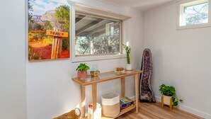 A room with a wooden console table, a window with a view of trees, a painting of a trail sign, and a cactus sculpture. - Guest House @ Juniper Ranch | Private, Views, King (Sedona)