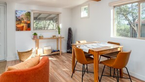 A dining area with a wooden table and orange chairs, a small shelf with decorative items, and a window with a view of trees. - Guest House @ Juniper Ranch | Private, Views, King (Sedona)