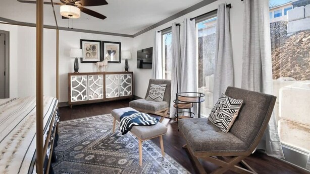Una sala de estar moderna con ventilador de techo, alfombra estampada, sofá, sillón y mesita auxiliar.