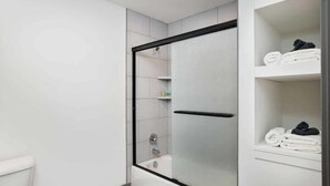Un baño moderno con ducha de vidrio, una bañera y un estante con toallas dobladas.