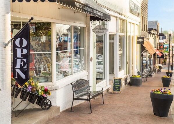 A storefront with a 'OPEN' sign, a bench outside, and potted plants on the sidewalk.