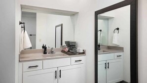 Une salle de bain moderne avec un grand miroir, des meubles blancs et une machine à café posée sur le comptoir.