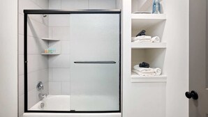 Un baño moderno con ducha de vidrio, azulejos blancos y puerta blanca.