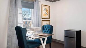 Un coin repas comprenant une table, deux chaises, un réfrigérateur et une fenêtre avec des rideaux.