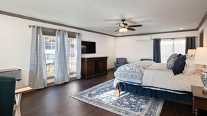 Une chambre à coucher comprenant un lit, un bureau, une chaise, un ventilateur de plafond, une télévision et une fenêtre avec des rideaux.