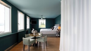 A modern hotel room with a bed, a television, a window, a table with chairs, and a curtain.