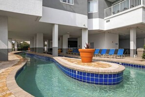 A swimming pool with a blue-tiled edge, surrounded by lounge chairs and a potted plant.