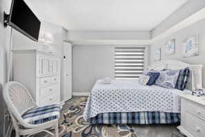 A bedroom with a bed, a dresser, a chair, and a television mounted on the wall.