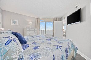 Une chambre à coucher avec un lit, une commode, un téléviseur et une vue sur l’extérieur.