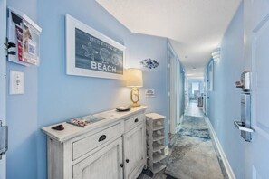A hallway with a light blue wall, a framed quote, a lamp, and a door with a key lock. - Oceanfront 3Bdrm Seaglass Escape-Lazy River,5 Beds (Myrtle Beach)