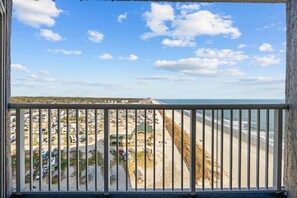 Een balkon met uitzicht op een strand en een parkeerplaats.