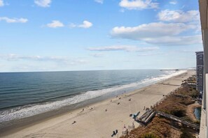 Een strand met een pier die zich uitstrekt over de oceaan, een zandstrand en een gebouw naast het strand.