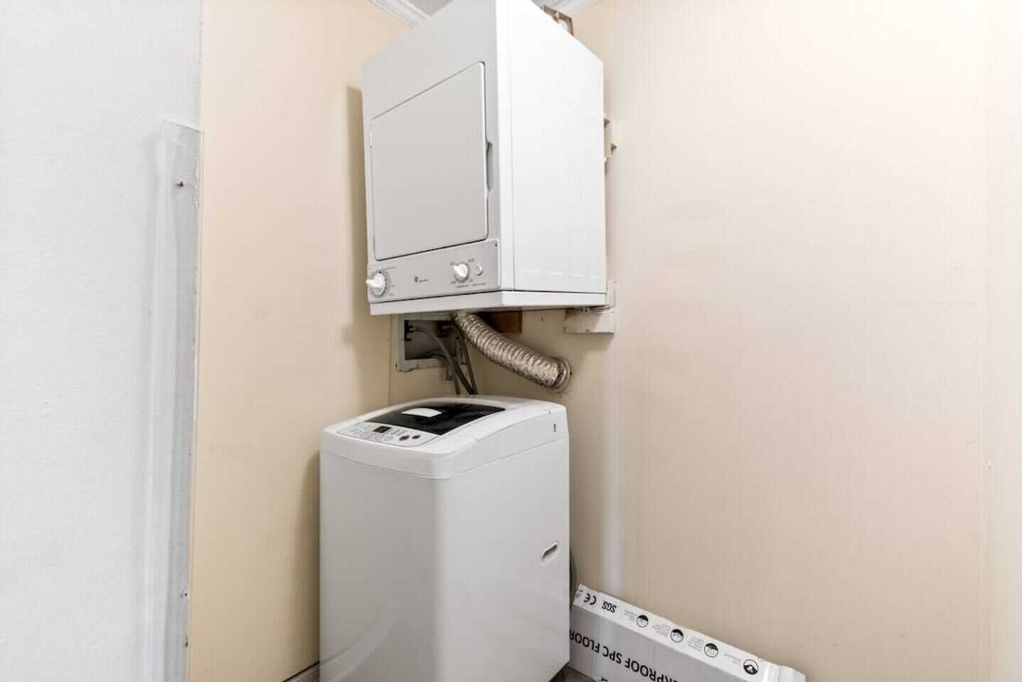 Máquina de lavar roupa compacta, branca e fixada à parede, com painel de controle e mangueira ligada a um respiradouro.