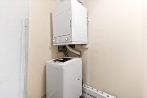 A compact, white, wall-mounted laundry machine with a control panel and a hose connected to a wall vent.