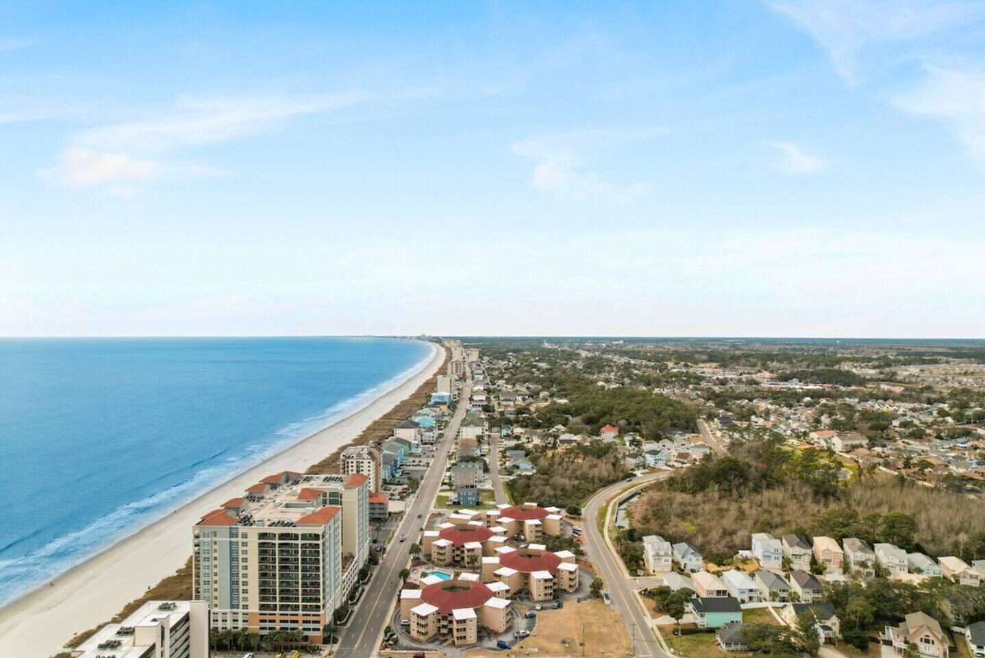 A coastal cityscape with a beach, residential buildings, and a road leading to a hotel area with multiple buildings.