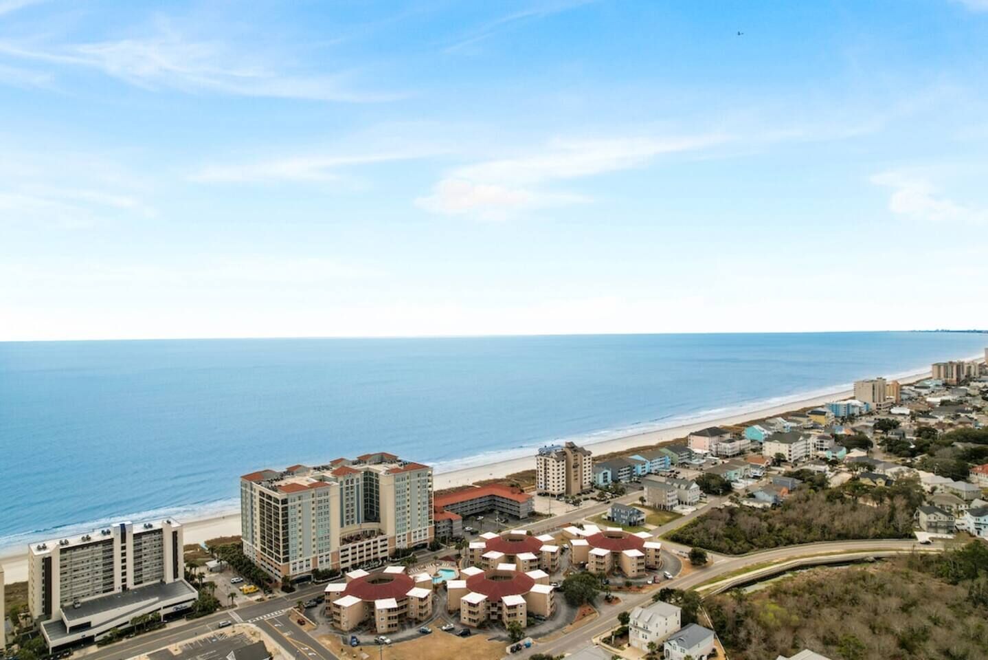 A coastal resort area with multiple buildings, including a prominent hotel with a red roof, situated near a beach.