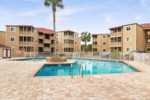 A pool area with a rectangular pool, surrounded by a paved deck, and adjacent multi-story buildings with balconies.