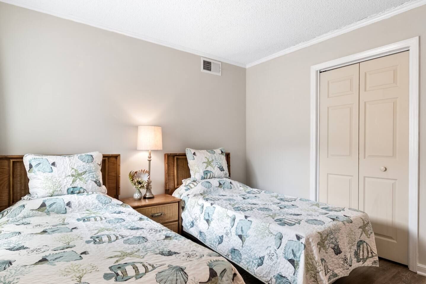 Quarto com duas camas, mesa de cabeceira e abajur, e uma porta.
