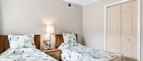 Quarto com duas camas, mesa de cabeceira e abajur, e uma porta.