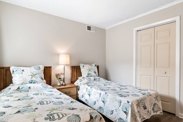 A bedroom with two beds, a nightstand with a lamp, and a door.