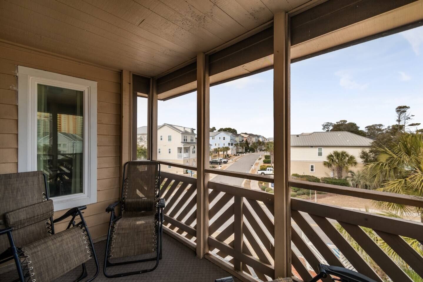 A covered balcony with two chairs, a window, and a view of a residential street.