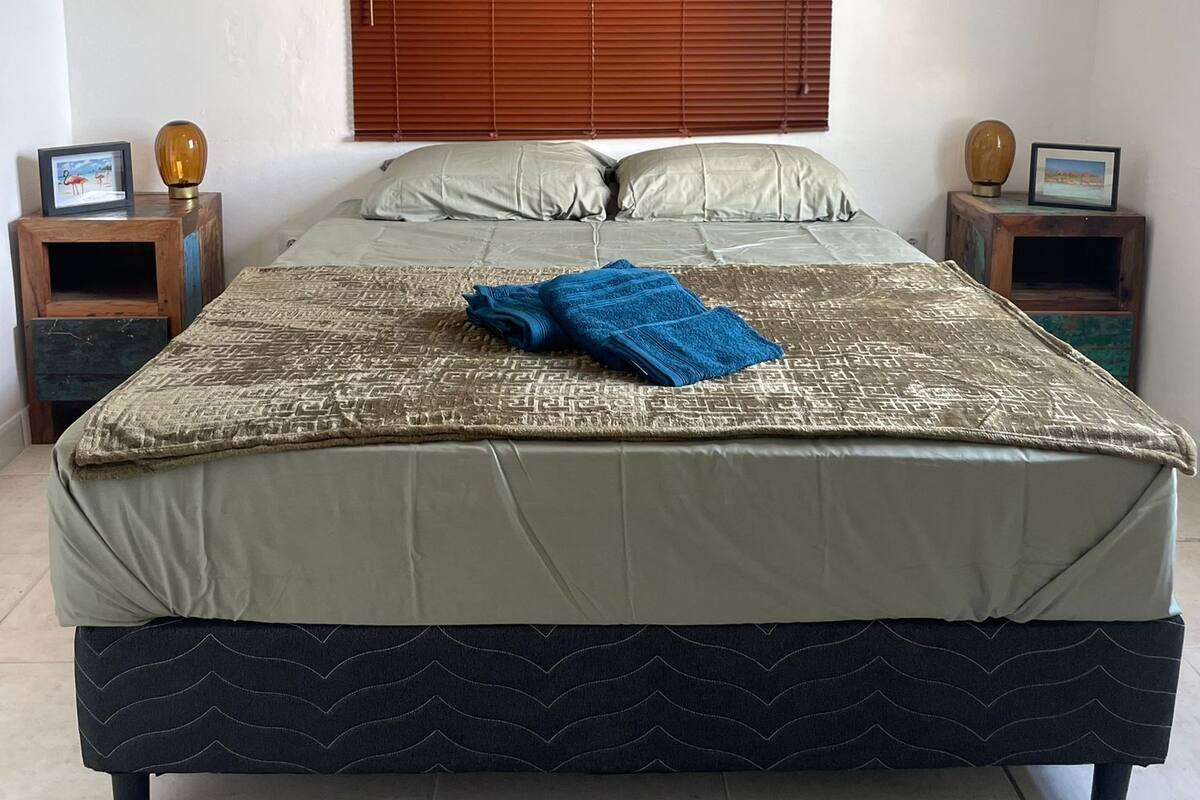 A bed with a patterned bedspread, two pillows, and a blue blanket. There are two nightstands with lamps and framed pictures.