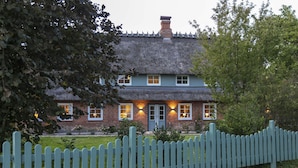 A traditional brick house with a thatched roof, a picket fence, and a well-maintained lawn. - Captains Lodge - Bathtub, Shower, Terrace, Grill, Secluded & Close to the Beach (Steinbergkirche)