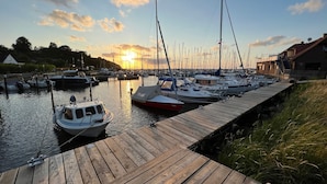 A marina with boats docked at wooden piers, a clear sky, and a sunset in the background. - Captains Lodge - Bathtub, Shower, Terrace, Grill, Secluded & Close to the Beach (Steinbergkirche)