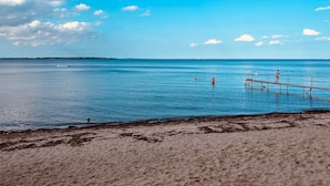 A beach with a wooden pier extending into calm blue waters, a sandy shore, and a clear sky with scattered clouds. - Captains Lodge - Bathtub, Shower, Terrace, Grill, Secluded & Close to the Beach (Steinbergkirche)